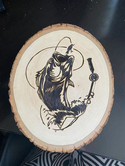 A Wood Slice With A Drawing Of A Fish Holding A Fishing Rod In Its Mouth