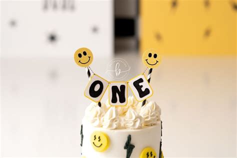 A White Cake With Yellow Smiley Faces And One Sign That Says One On It