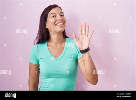 Young Hispanic Woman Standing Over Pink Background Waiving Saying Hello