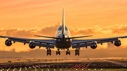 An Airplane Is Taking Off From The Runway At Sunset Or Dawn With Clouds