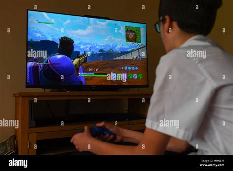 A teenager boy plays the hit computer game Fortnite on a large TV on a ...