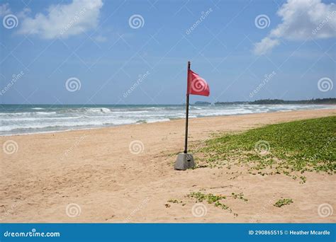 Red Warning Flag Set In Concrete On Sandy Beach With Powerful Ocean Waves In Background Stock