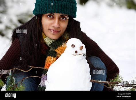 A Woman Wearing A Hat And Scarf With A Snowman Outdoors In The Forest