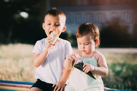 Hermano Y Hermana Comiendo Helado En El Banco Del Patio De Juegos Es