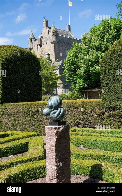 A Historic Castle In The Background With A Sculpture In A Formal Garden