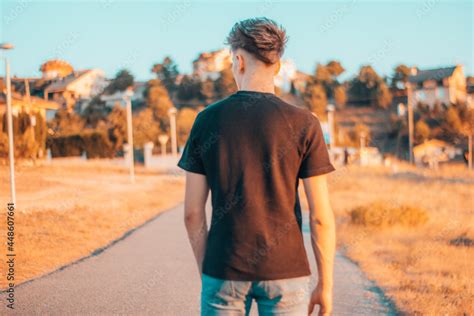 Chico joven de espaldas caminando hacía la ciudad en la carretera Stock