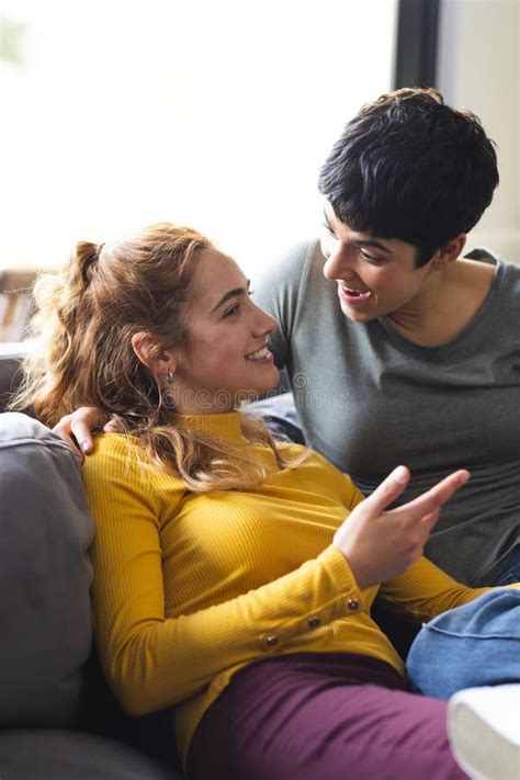 Happy Biracial Lesbian Couple Embracing On Couch And Talking In Sunny