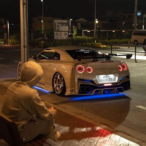 a person sitting on a bench in front of a car with its lights on at night