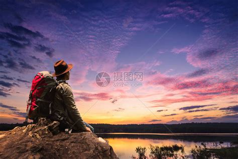 男子在山顶河边远足和背包背着包的旅行者年轻人日落时分坐在悬崖高清图片下载 正版图片506519221 摄图网