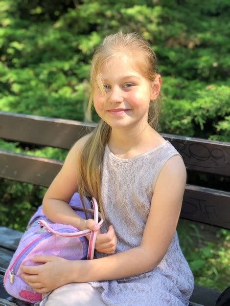 Premium Photo Portrait Of Smiling Girl Holding Bag While Sitting On Bench At Park