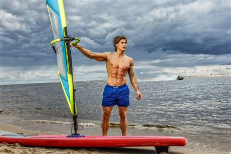 Surfer Male With A Muscular Body With His Surfboard At The Beach Stock