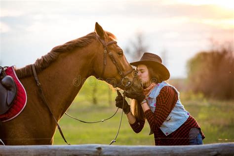 A Cowgirl Stands Near Her Horse In A Field At Sunset Stock Image