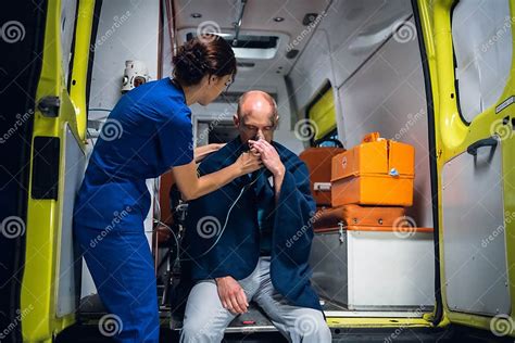 Young Nurse In Uniform Puts Oxygen Mask On Man Sitting In Blanket In