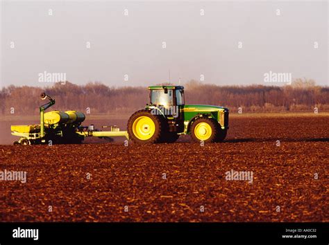 A John Deere Tractor And Planter Plant Grain Corn In The Fertile Soil