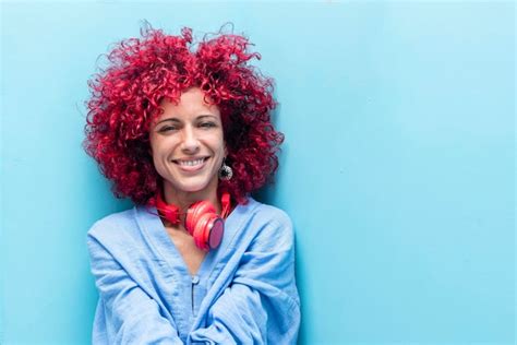Uma jovem latina sorridente um cabelo afro vermelho em fundo azul olhando para a câmera