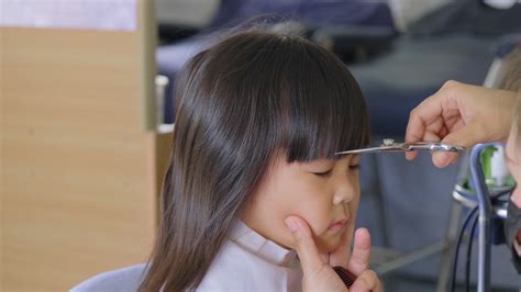 Asian little girl gets her hair cut at a beauty salon by a hairdresser ...