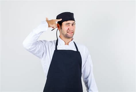 Chef masculino tocando a cabeça gesto de arma de uniforme vista