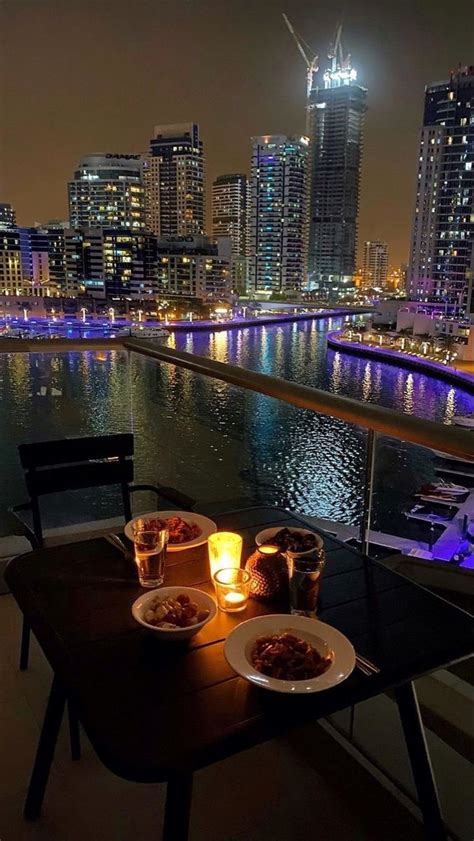 Two Plates Of Food Sit On A Table Overlooking A River And City Lights