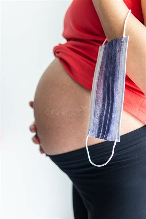 Pregnant Woman Shows Her Belly While Holding A Medical Protective Face