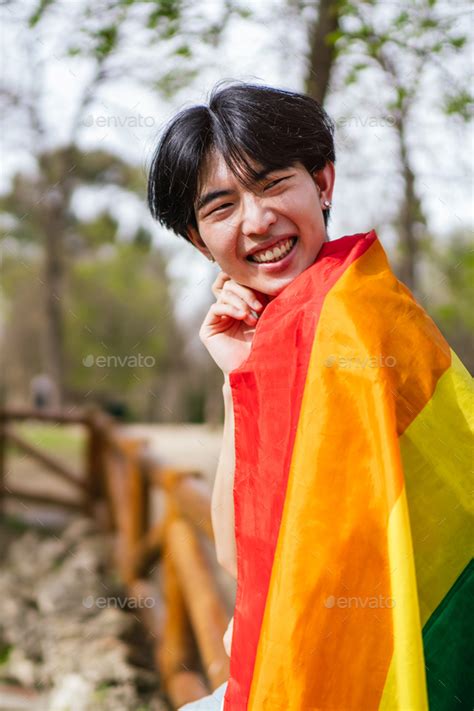 Smiling Chinese Gay Man Wrapped In Rainbow Flag Enjoying Outdoors