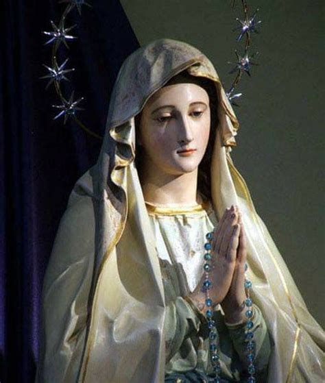 A Statue Of The Virgin Mary Holding Her Hands Together With Blue Beads