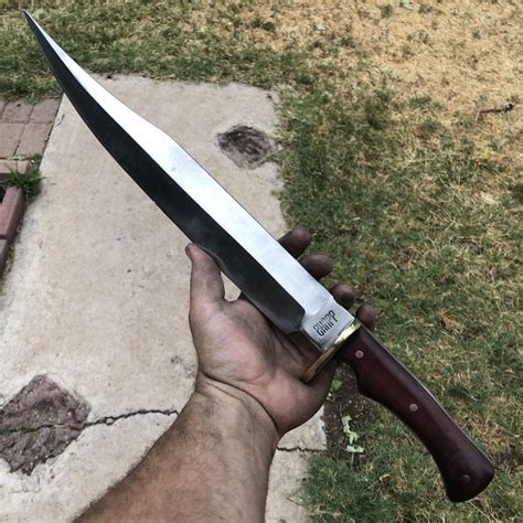 a hand holding a large knife on top of a stone slab in front of grass