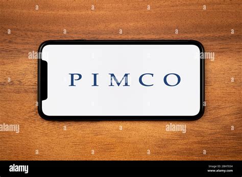 A smartphone showing the Pimco logo rests on a plain wooden table (Editorial use only Stock ...