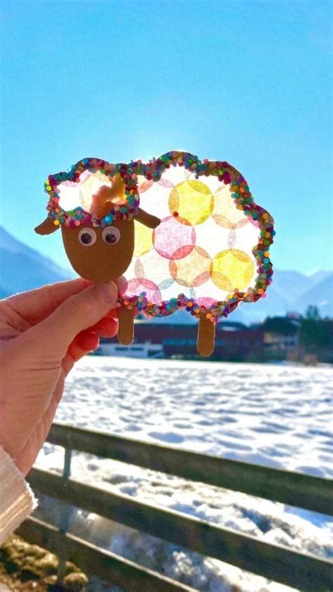 A Hand Holding Up A Paper Sheep On Top Of Snow Covered Ground With