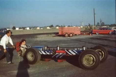 Two Men Are Standing Next To An Old Race Car In A Parking Lot With