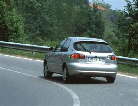 A Silver Car Driving Down The Road Next To Some Trees And Bushes On