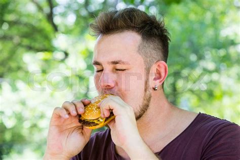 emotional young guy eating a cheeseburger on the nature | Stock image ...