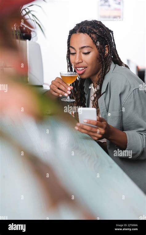 African American Woman Holding Glass Of Cocktail And Using Blurred