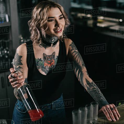 Tattooed Bartender Holding Bottle Of Alcohol And Looking Away Stock