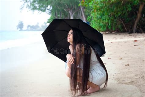 Young Woman On Beach Holding Umbrella Looking Up At Rain Stock Image