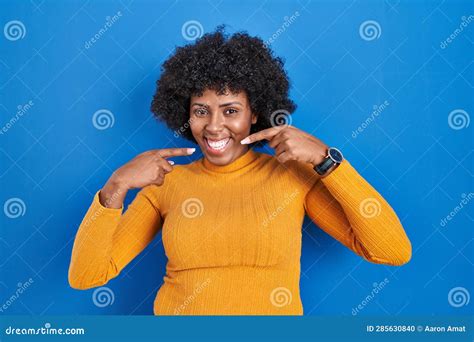 Black Woman With Curly Hair Standing Over Blue Background Smiling Cheerful Showing And Pointing