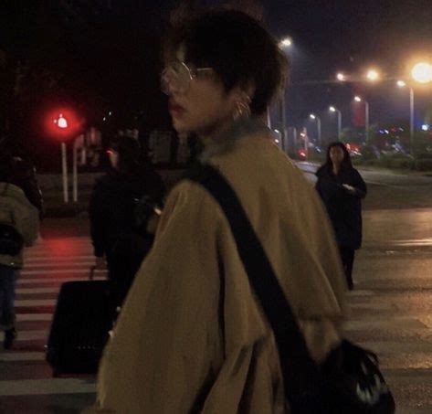 A Woman Walking Across A Street At Night With Her Hand In Her Pocket