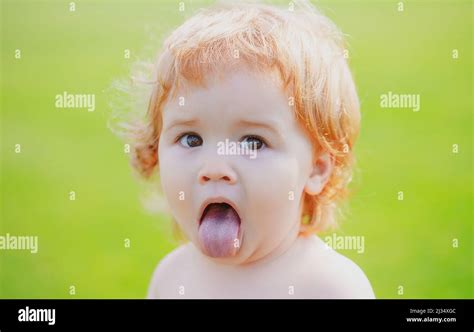 Funny child in park. Baby face with tongue close up. Funny little child closeup portrait. Blonde ...