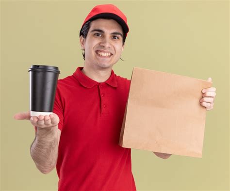 Sonriente joven repartidor caucásico en uniforme rojo y gorra