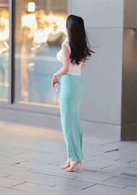 A Woman Is Standing On The Sidewalk With Her Back To The Camera And Looking At Something