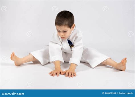 A 5 Year Old Boy Practices Karate Stretches His Legs On A White