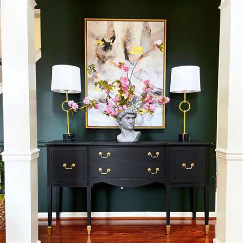 A Black Dresser With Flowers On Top And Two Lamps Next To It In Front