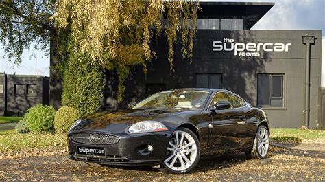 A Black Sports Car Parked In Front Of A Building With The Supercar Logo