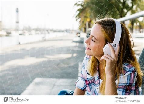 Junge blonde Frau hört Musik über Kopfhörer während sie im Skateboard