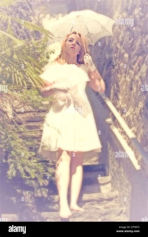 Young Woman Standing On A Staircase And Holding A Parasol And A Fan Her