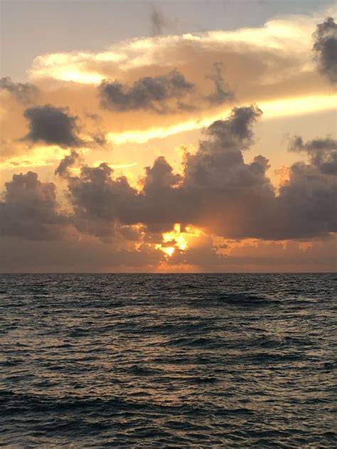 The Sun Is Setting Over The Ocean With Clouds In The Sky And On The Water