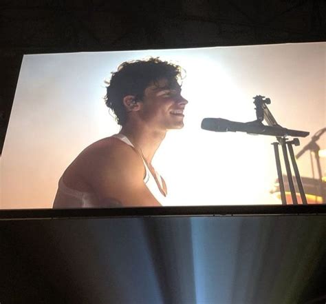 A Man Standing Next To A Microphone In Front Of A Large Screen With An