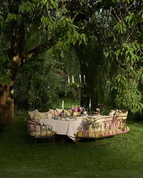 An Outdoor Dining Table Set Up In The Grass Under A Tree With Candles