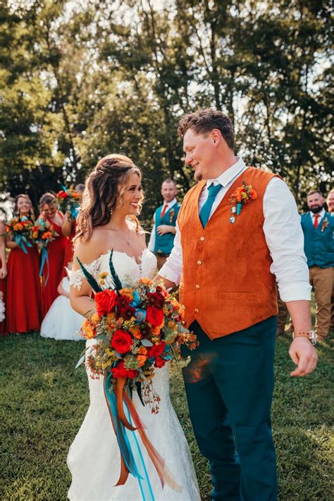 A Bride And Groom Standing In Front Of A Group Of People Wearing Orange