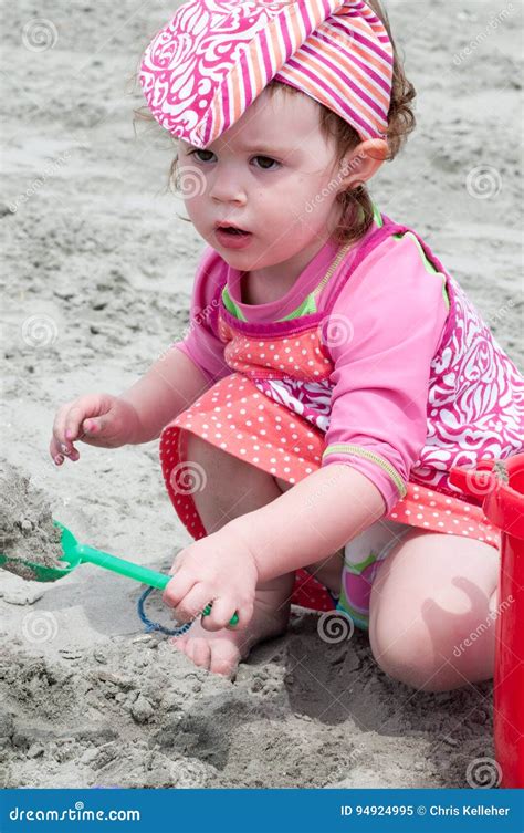 Young Little Girl Playing With The Sand And Building Sandcastle At The