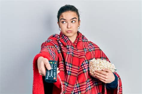 Young Caucasian Girl Wearing Blanket Eating Popcorn Using Tv Control